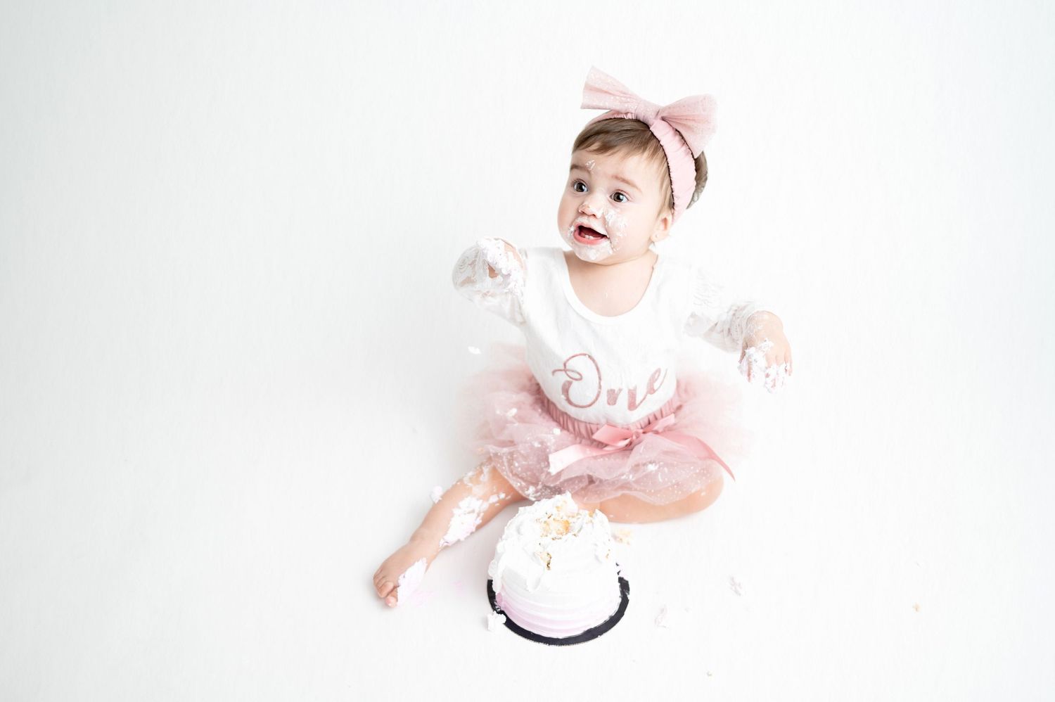 Baby in pink and white outfit sitting on floor during photoshoot.
