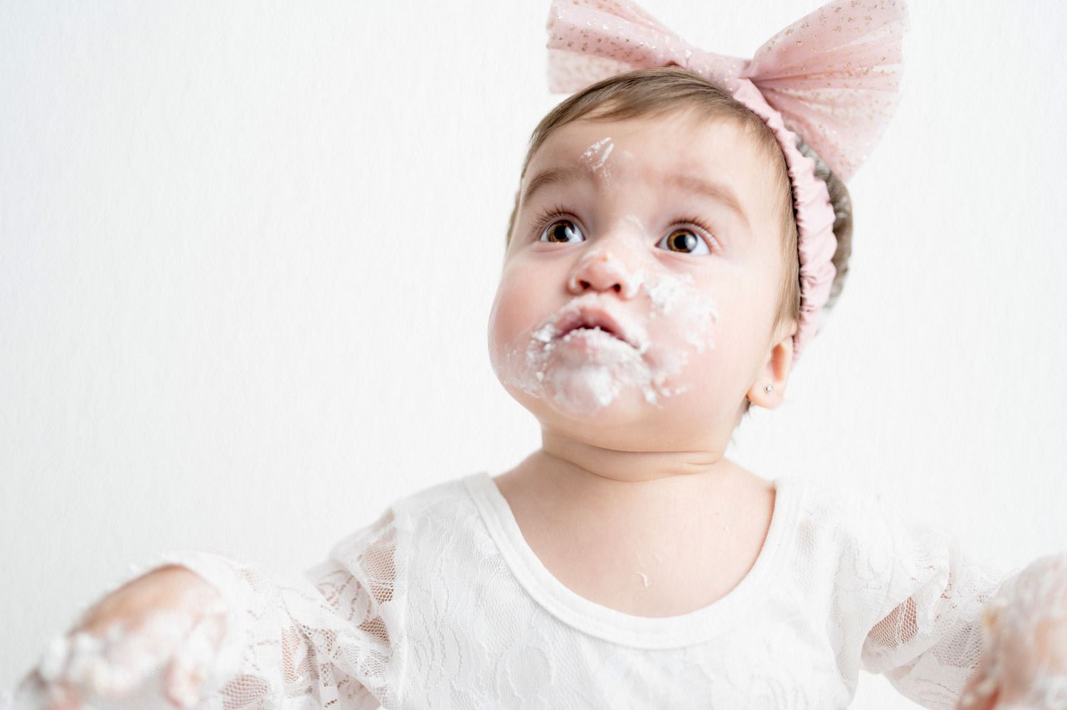 Baby with messy face wearing pink bow during cake smash photo session.