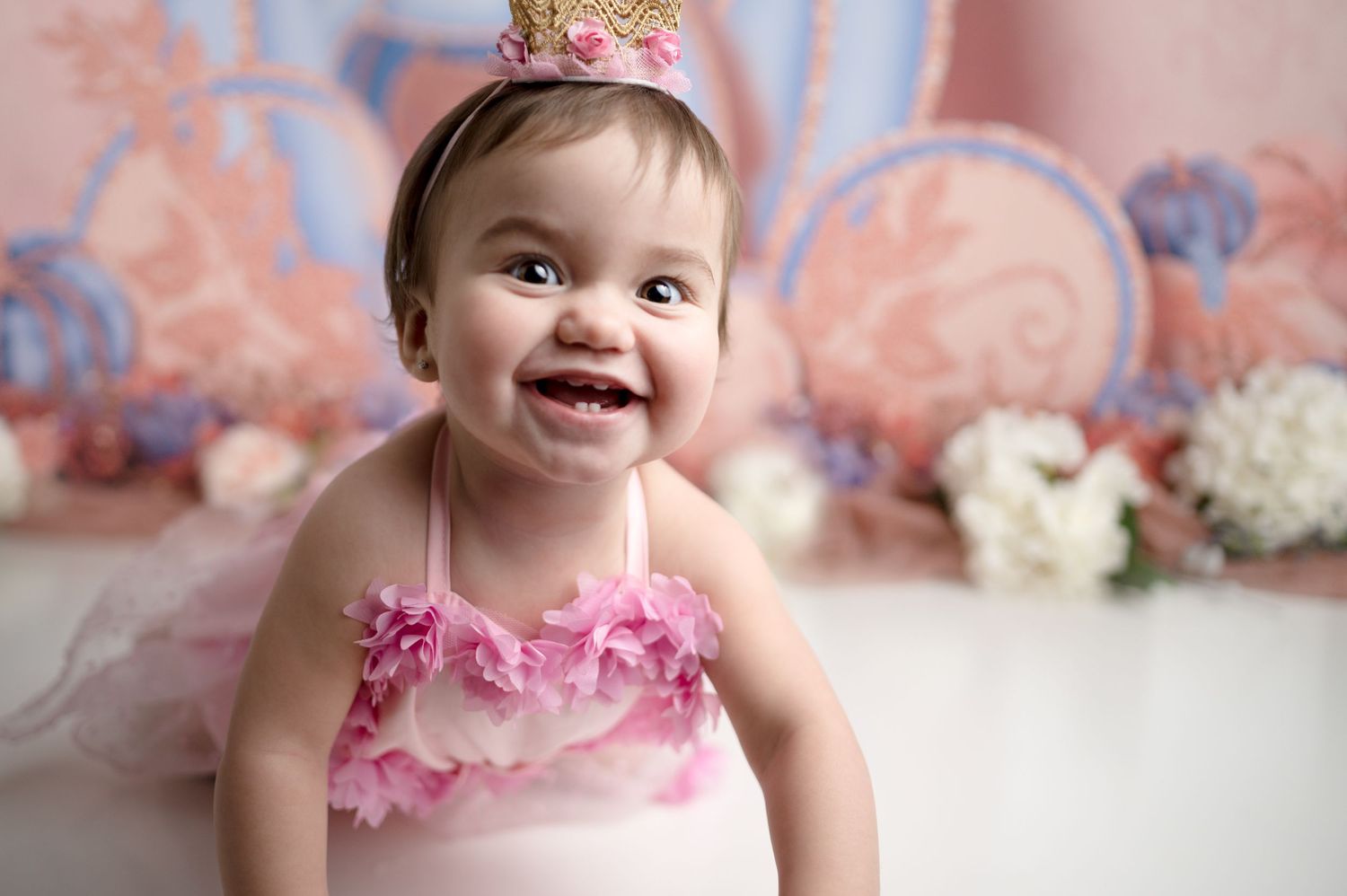 Baby in pink dress and crown smiling during first birthday photoshoot.