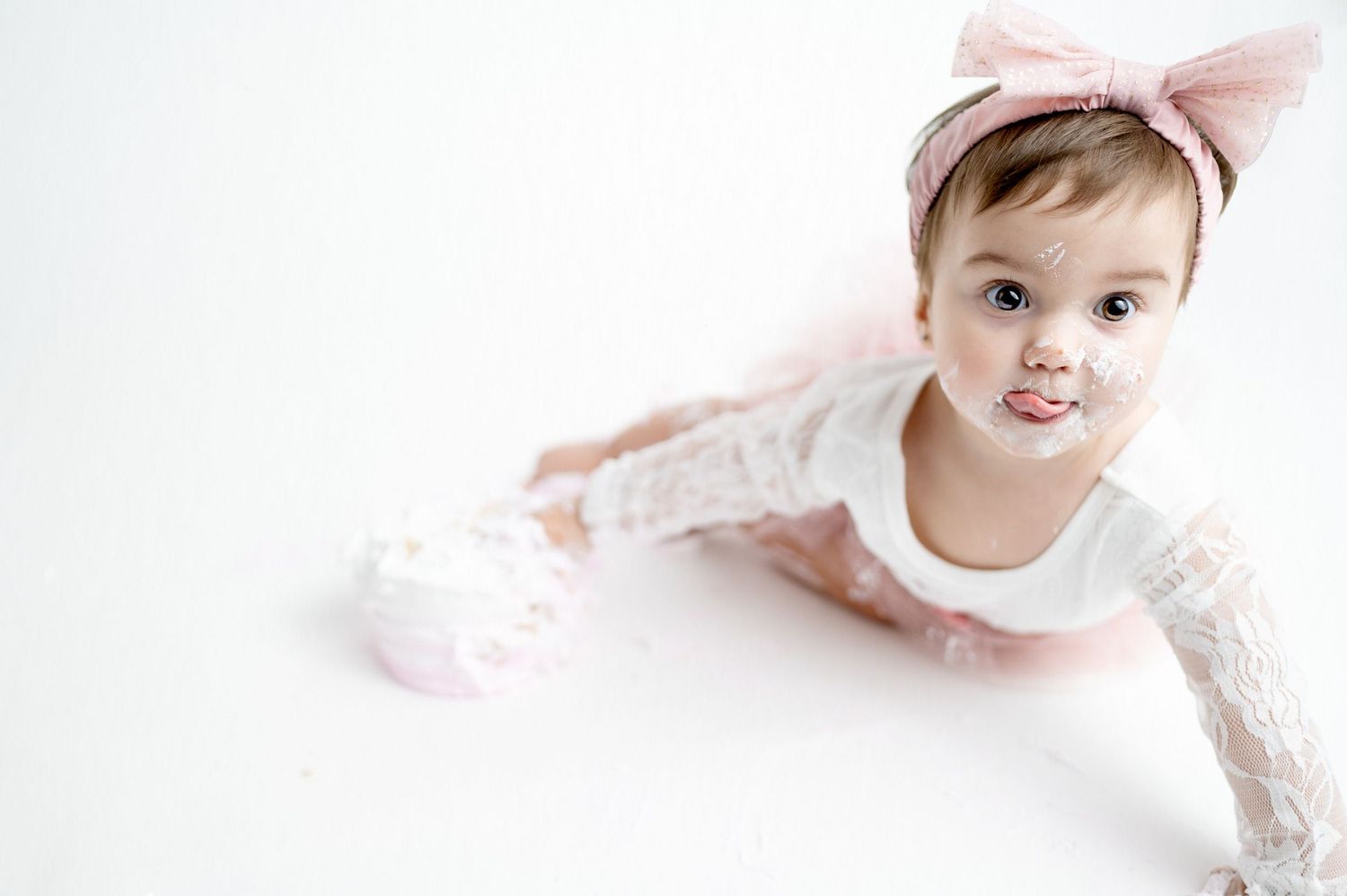 Baby wearing pink bow and white outfit crawling on white floor.