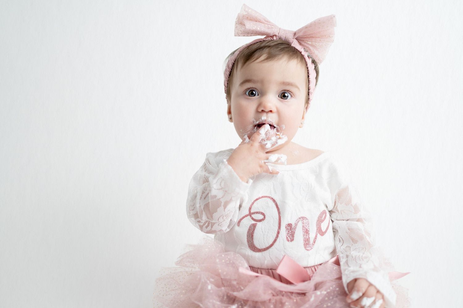 Baby in pink tulle dress with frosting on face during cake smash photo session.