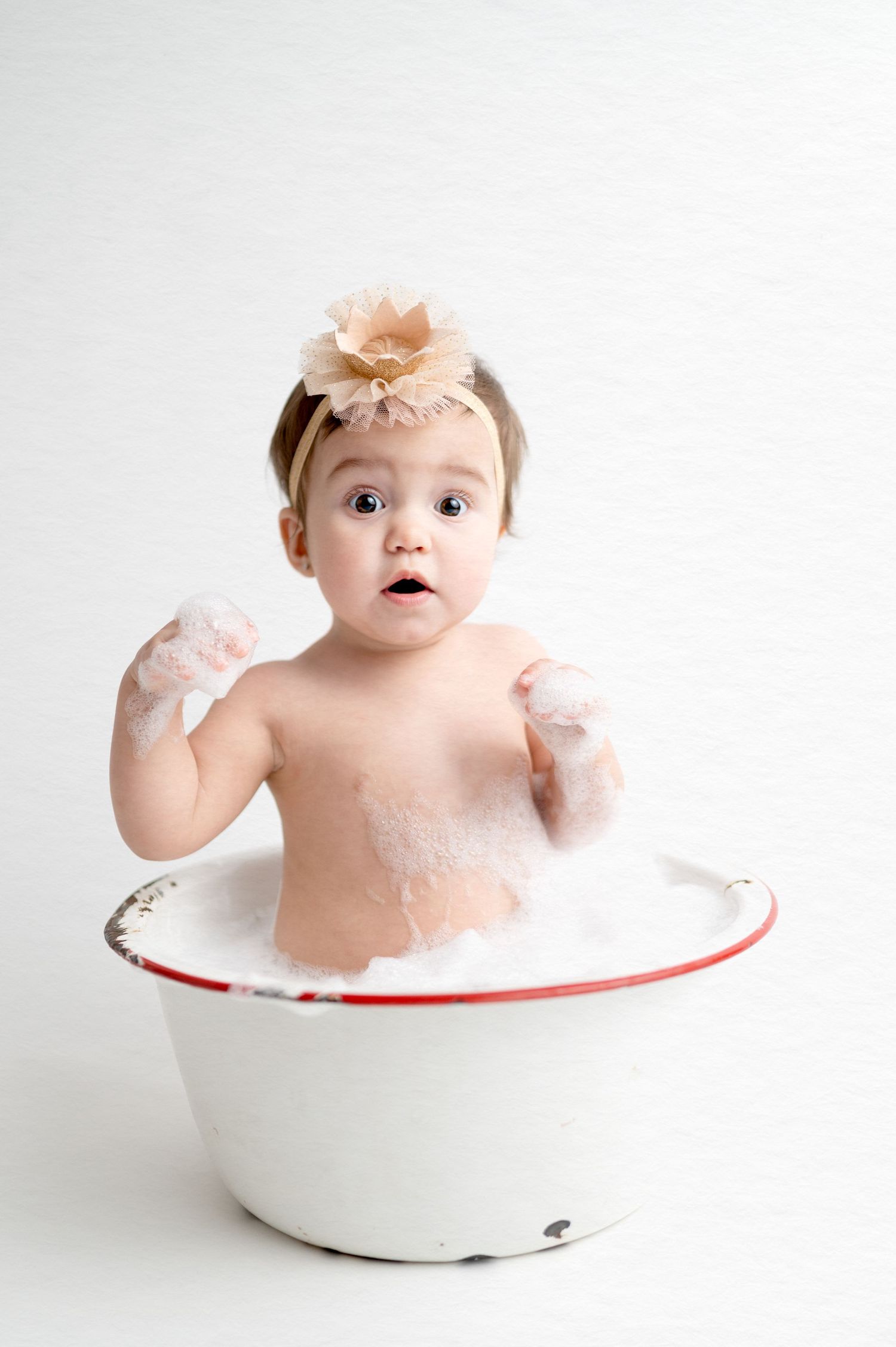 Baby in vintage enamel tub with soap bubbles wearing peach crown.