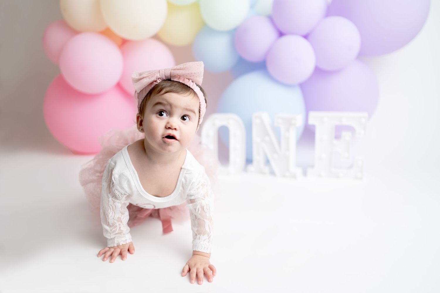 Baby crawling under pastel balloon arch during first birthday photo session.