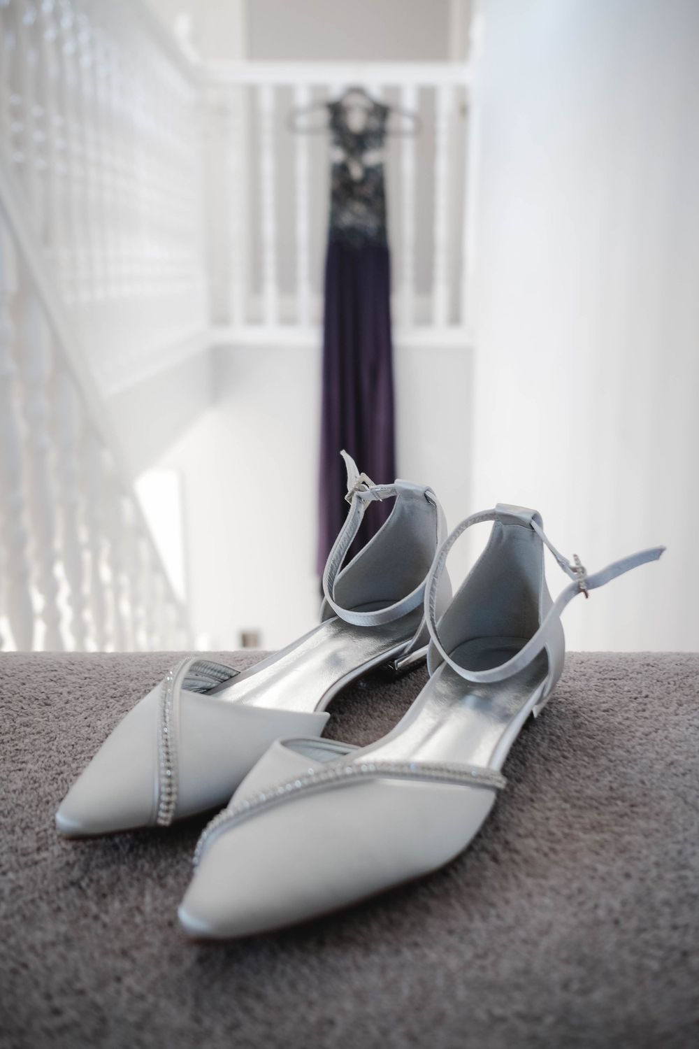 White pointed-toe flats with ankle straps displayed on grey carpet near dress.