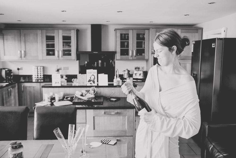 Person in white robe examines champagne bottle in modern kitchen setting.