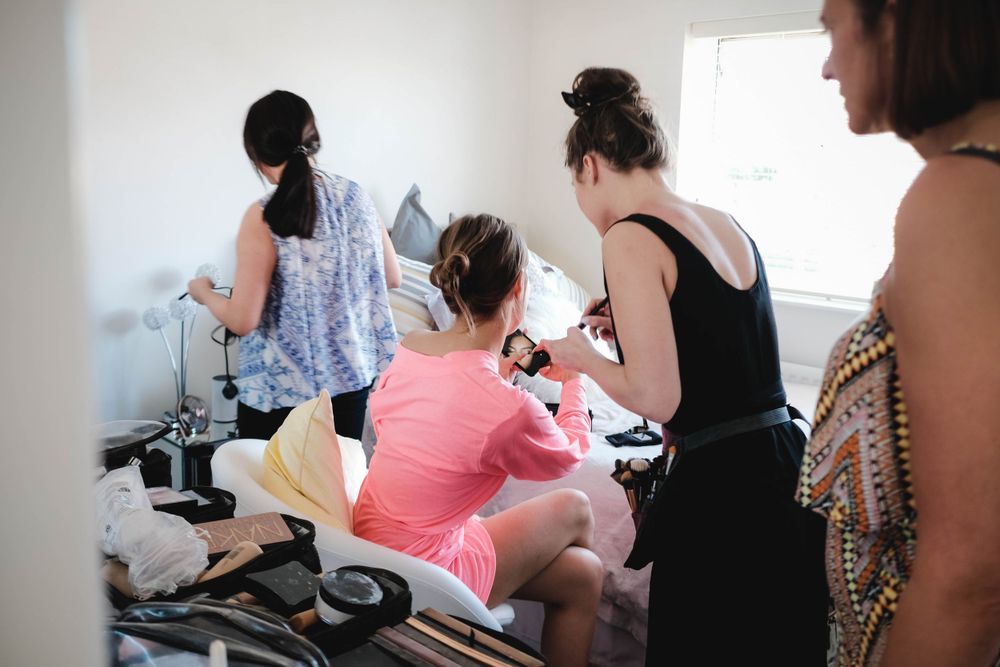 Group getting ready in preparation room with makeup and styling tools visible.