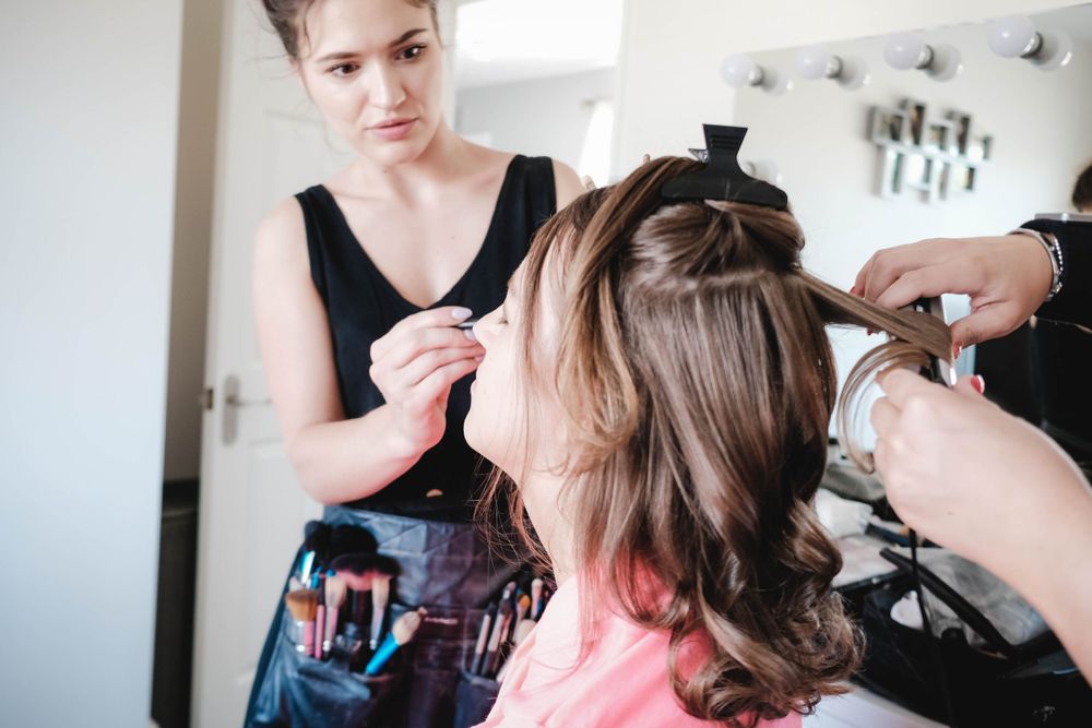 Hairstylist in black uses tools to style client's hair in bright salon setting.