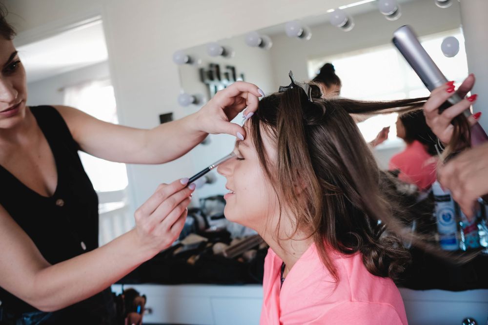 Stylist works on sectioning and styling hair while client wears pink top.