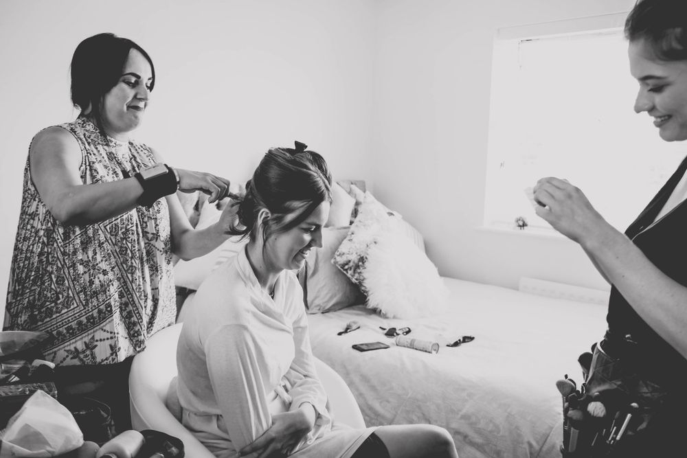 Black and white photo of preparation session with stylists working on formal hairstyle.