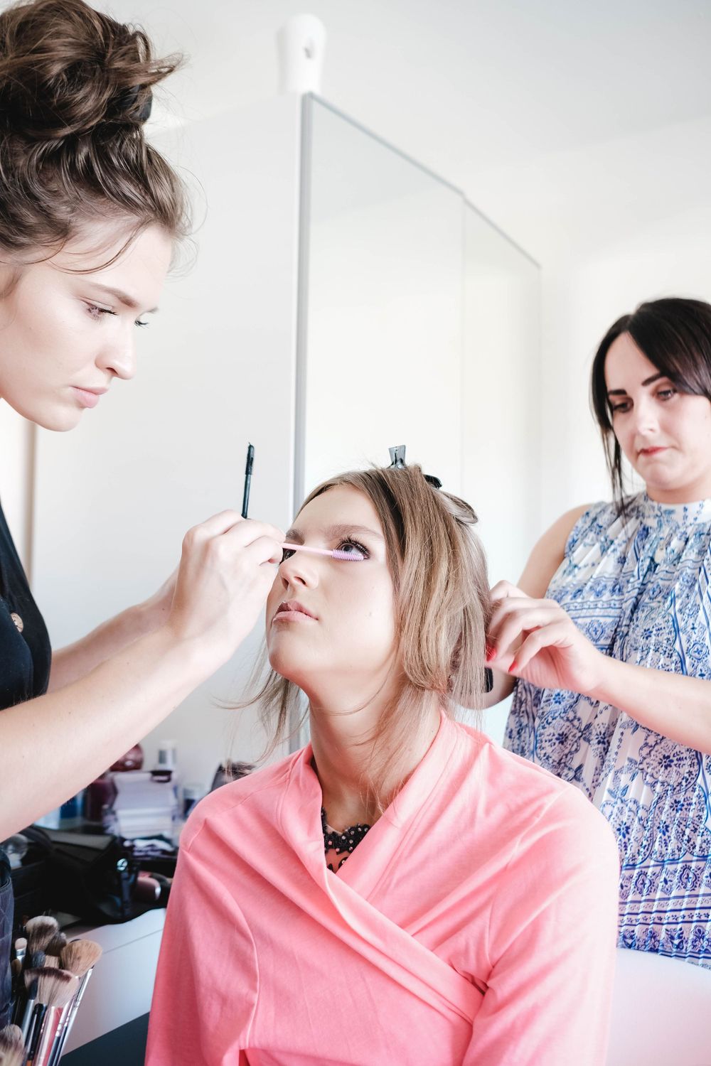 Professional makeup application session in a bright white room with multiple stylists working.