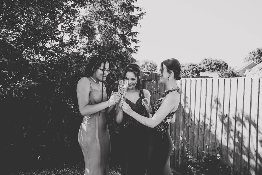 Black and white photo of three people in formal attire sharing a moment in a backyard.