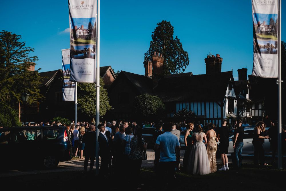 Wedding guests gathered outside a historic venue with flags and Tudor-style architecture.