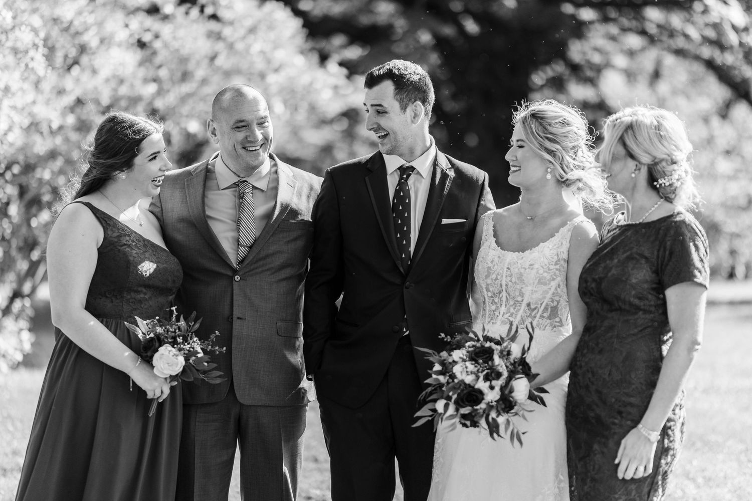 Black and white photo of wedding party sharing laughs outdoors.