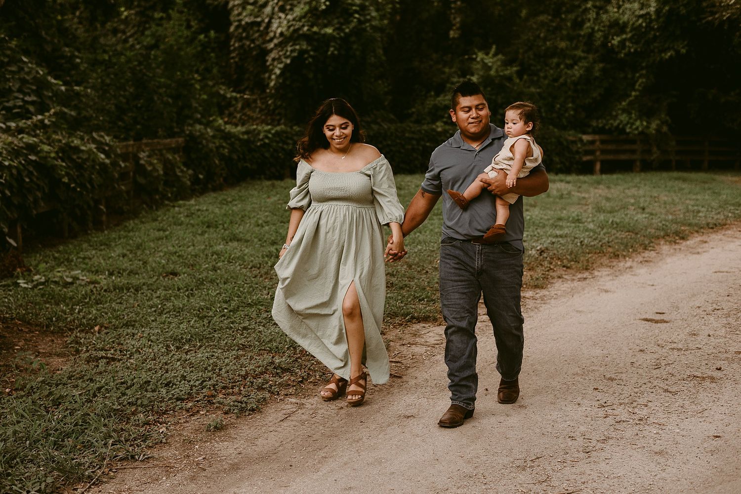 Family walks together on wooded path with parent carrying toddler.