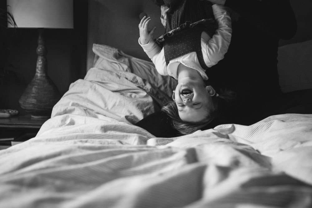 Black and white photo of playful bedtime moments with white bedding.