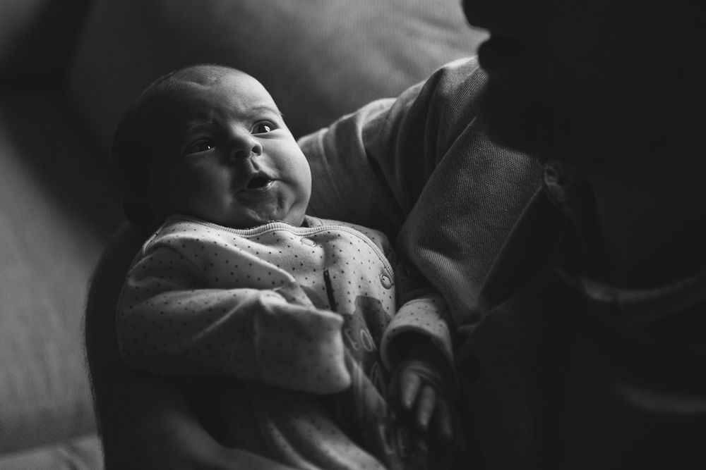 A black and white portrait of an infant lying down with outstretched arms.