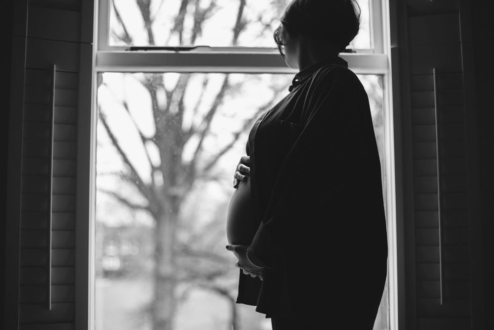 Silhouette of an expectant mother standing by a window in black and white.