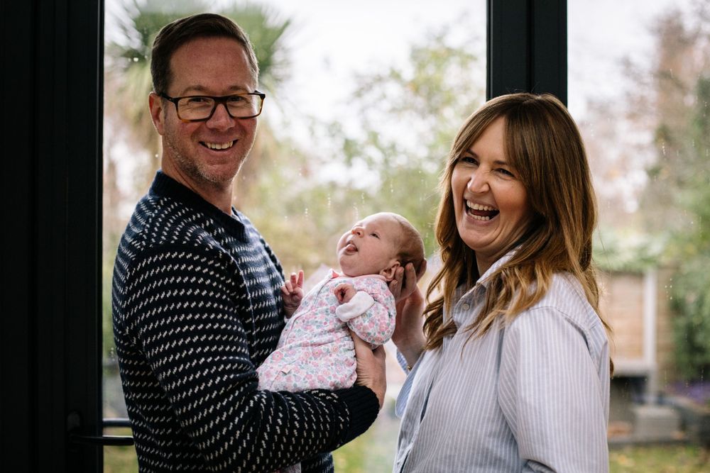 A joyful family moment with a newborn baby captured by a window.