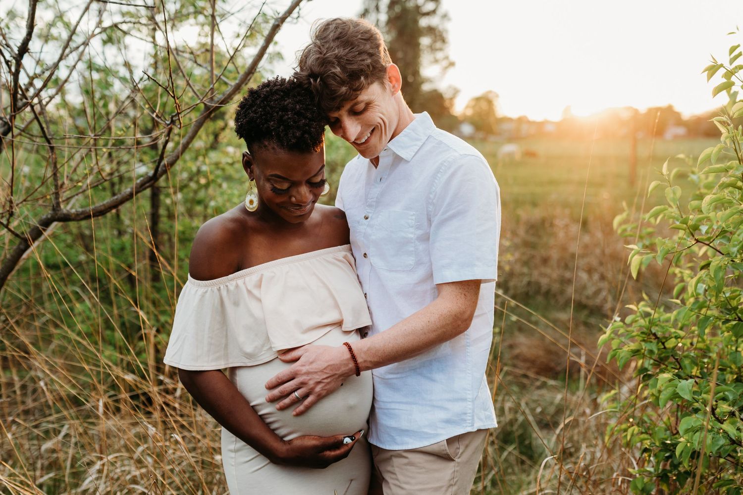 Husband and wife stand looking at wife's pregnant belly and smiling