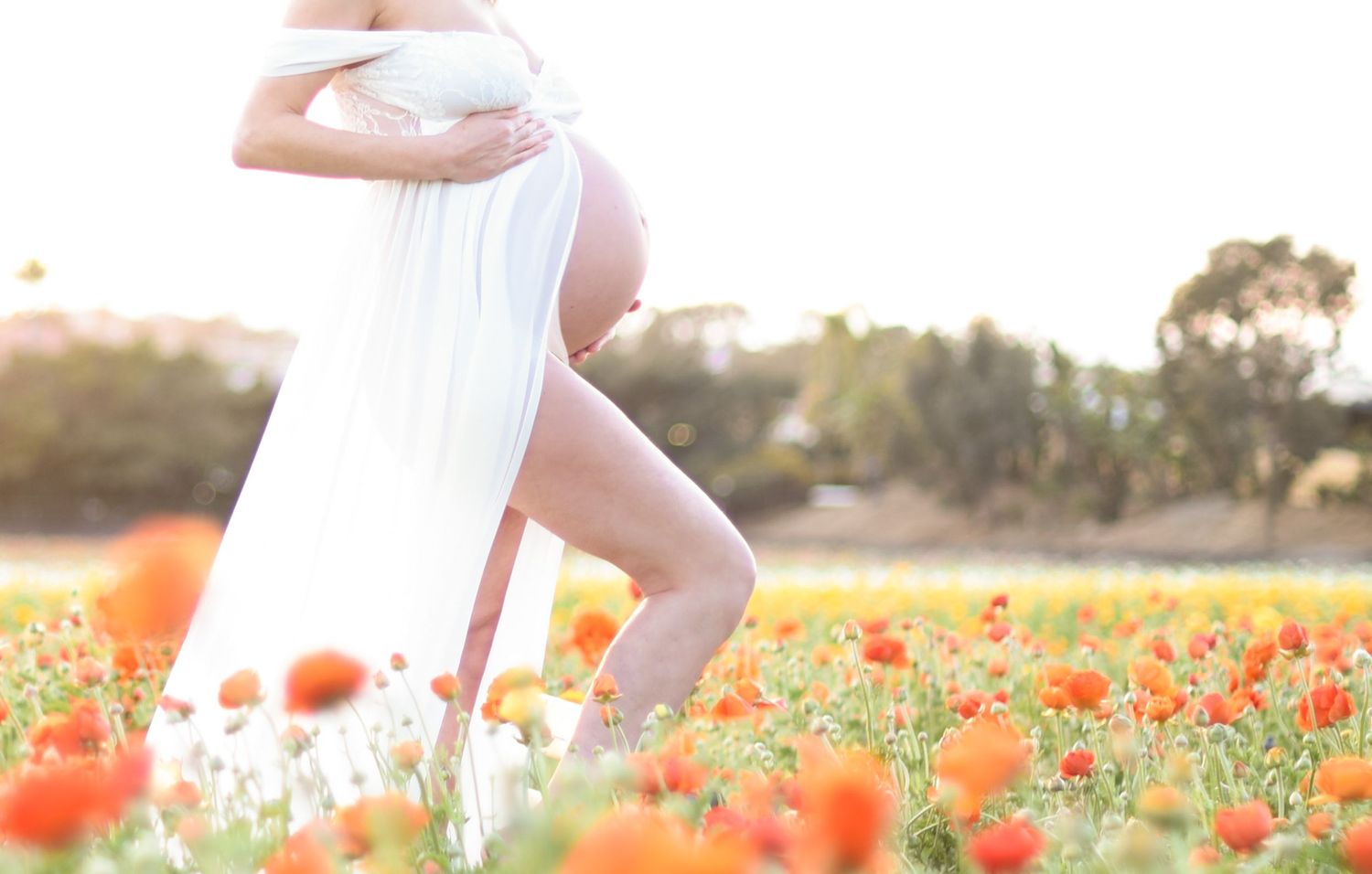 Woman in flowing white dress walking through vibrant orange poppy field at sunset.