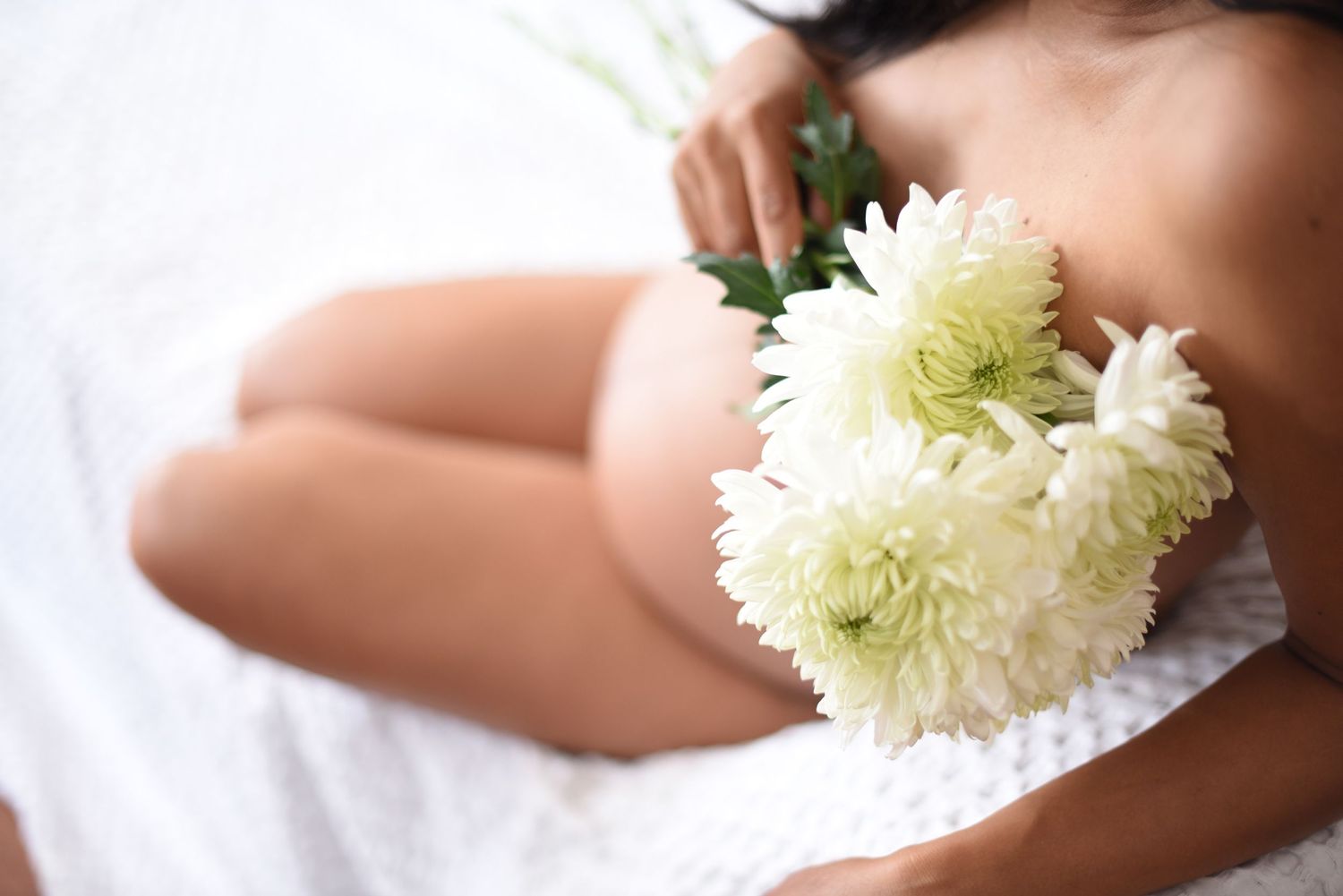 Artistic maternity photo with white chrysanthemums against light background.