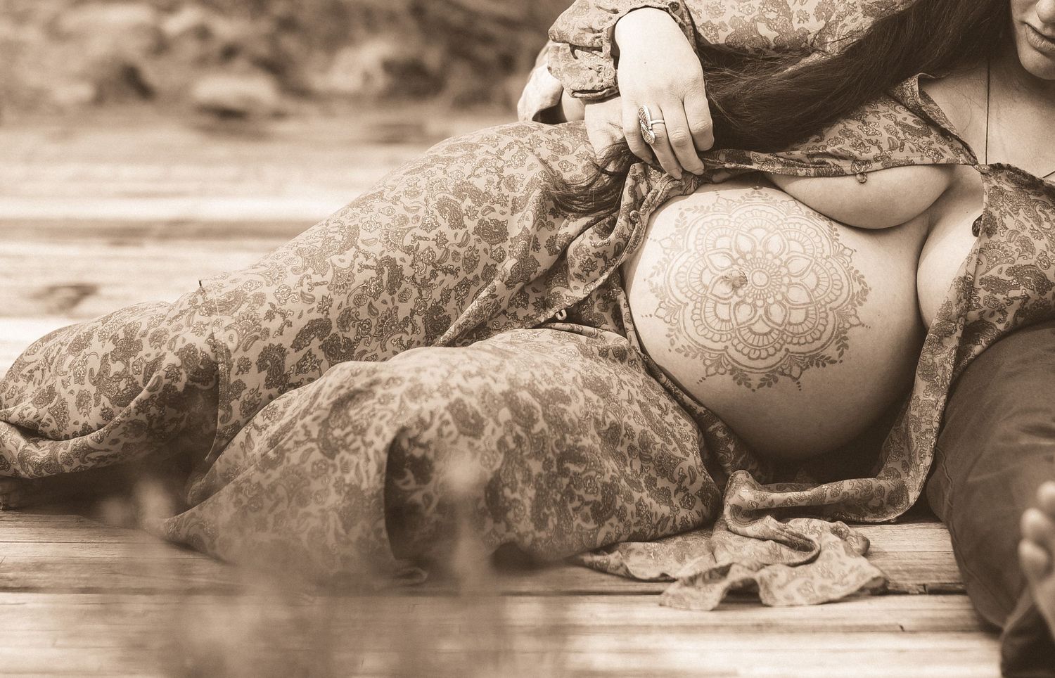 Artistic sepia photo of decorated pregnant belly resting on beach rocks.
