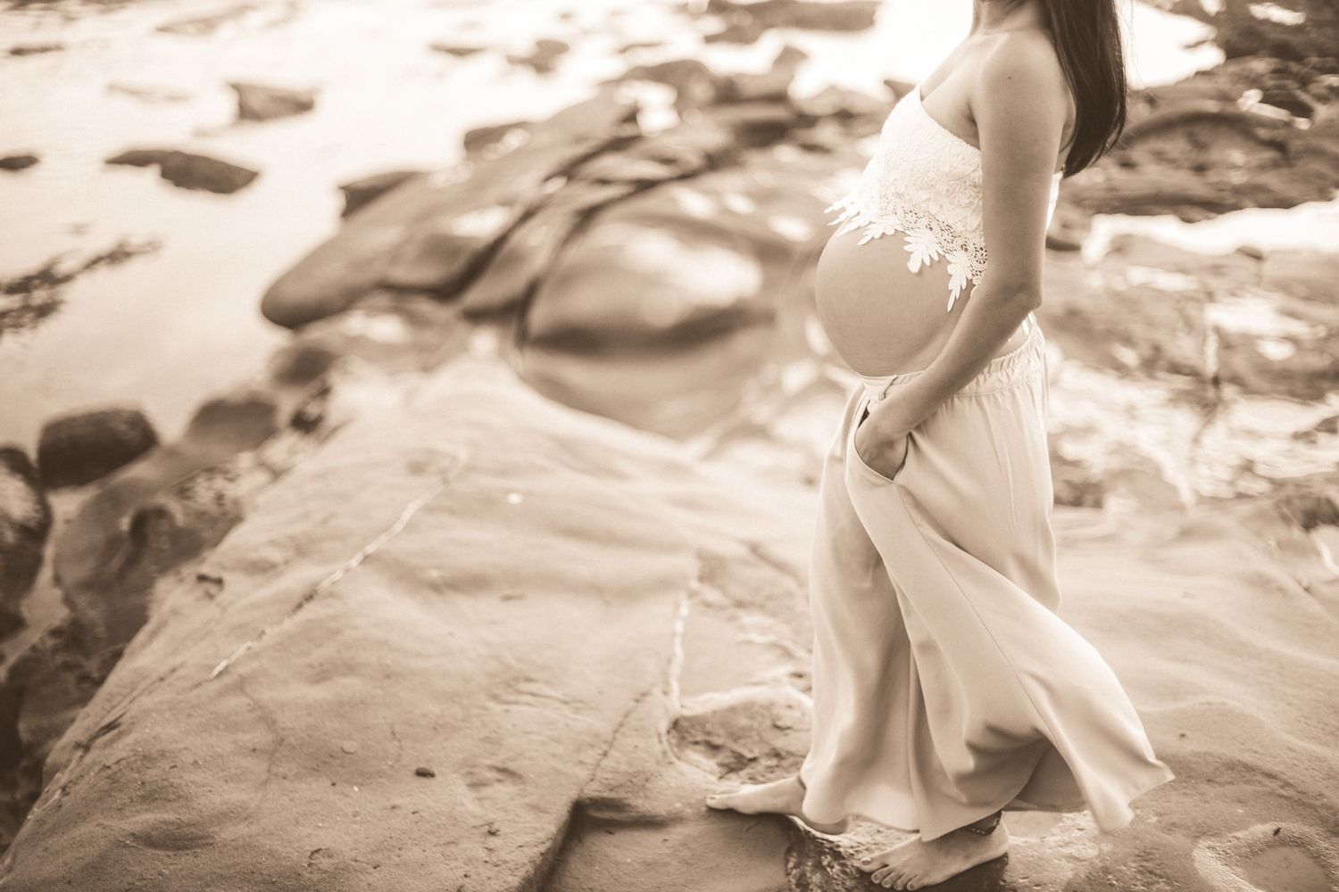 Romantic beach maternity photoshoot featuring flowy white dress against golden sunset background.