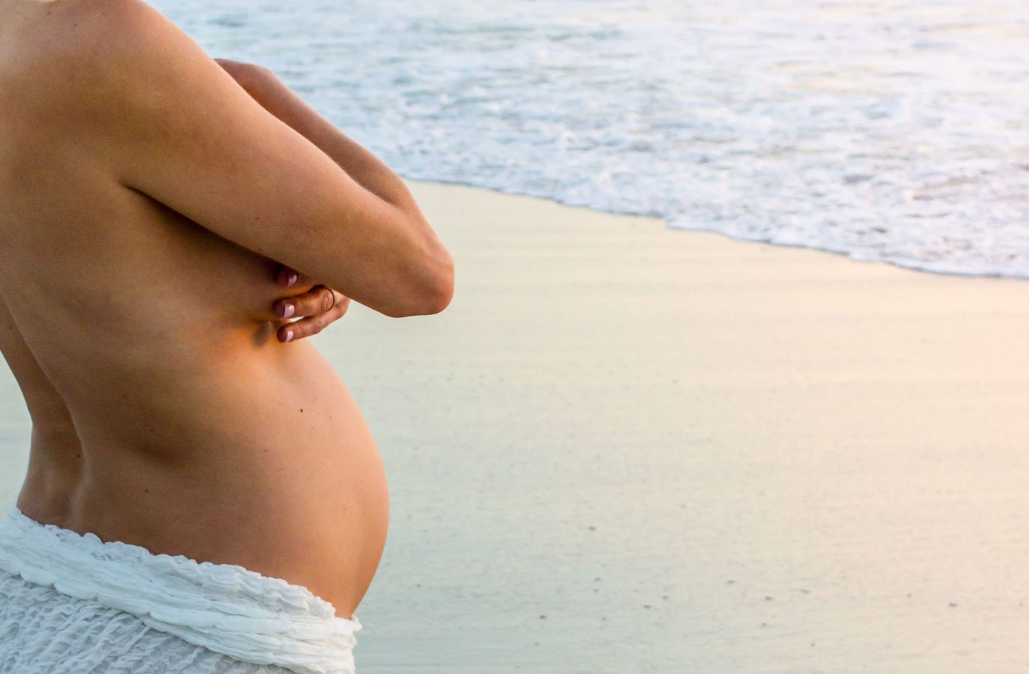 Close up of pregnant belly against beach and ocean background.