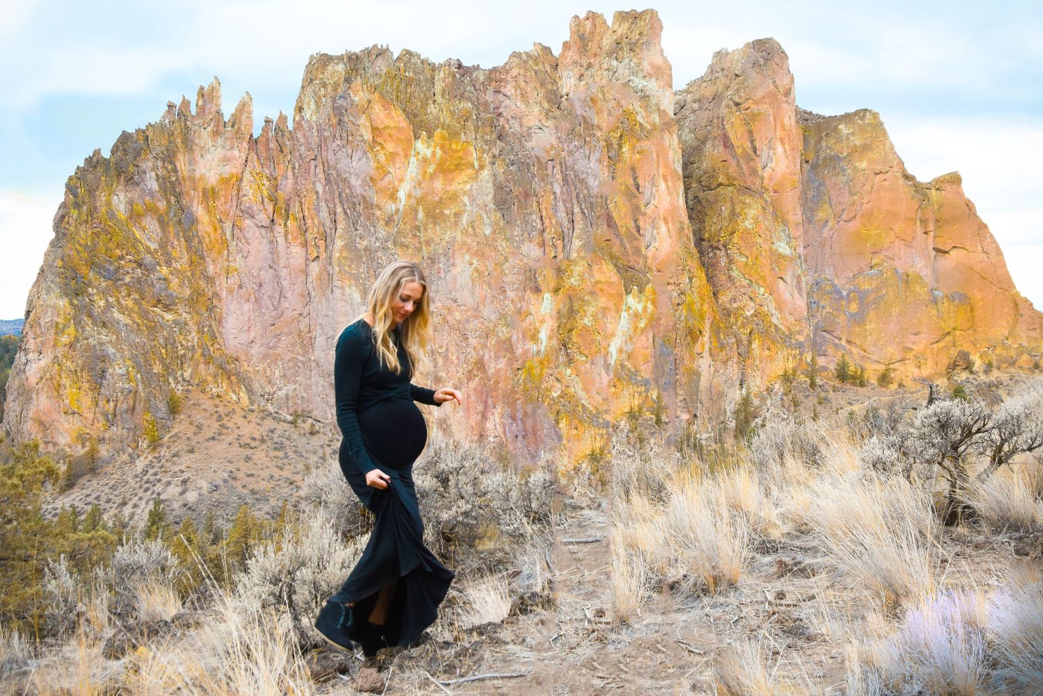 A woman poses in front of dramatic orange rock formations in a desert landscape.