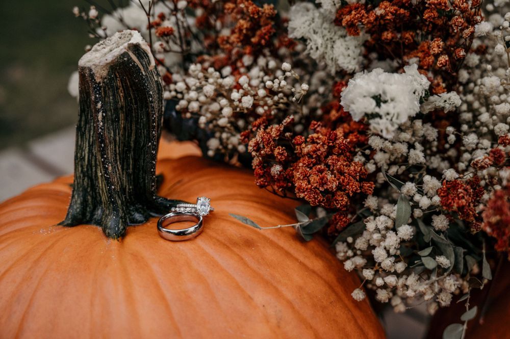 Diamond engagement ring resting on an orange pumpkin surrounded by a rustic fall bridal bouquet.