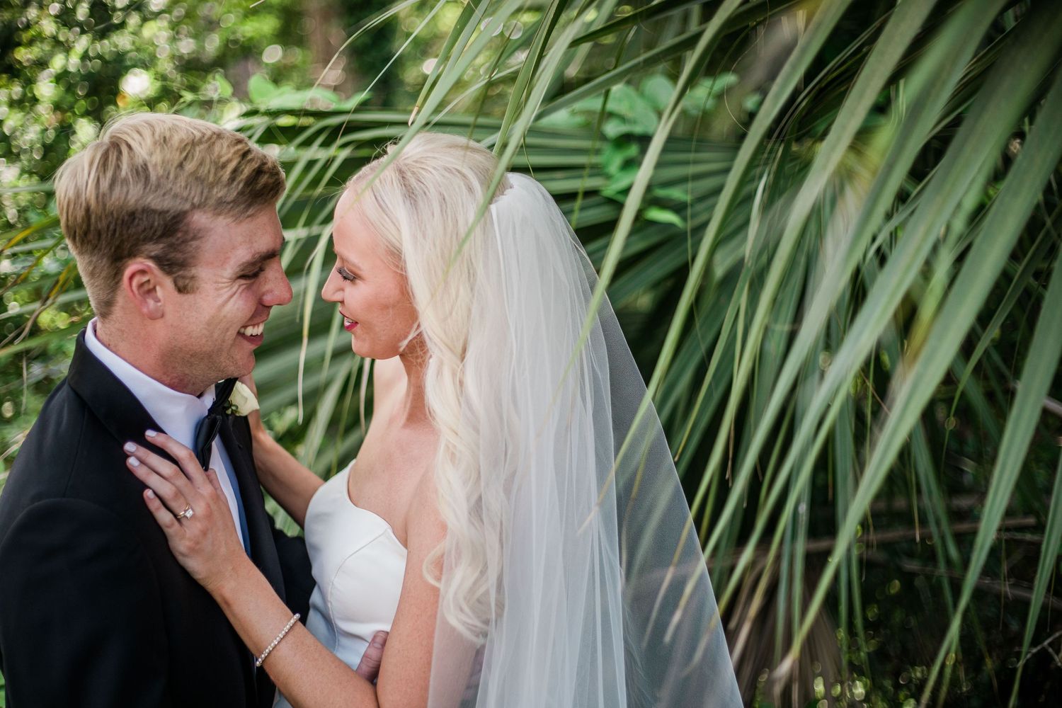 An intimate wedding portrait captured against a backdrop of palm leaves.