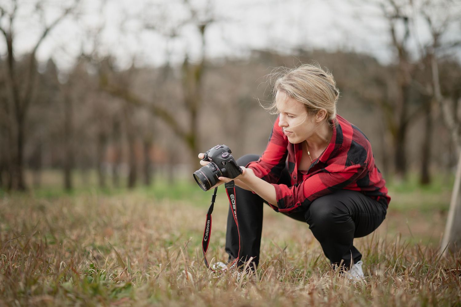 Professional photographer in red plaid shirt working outdoors in a field of tall grass.