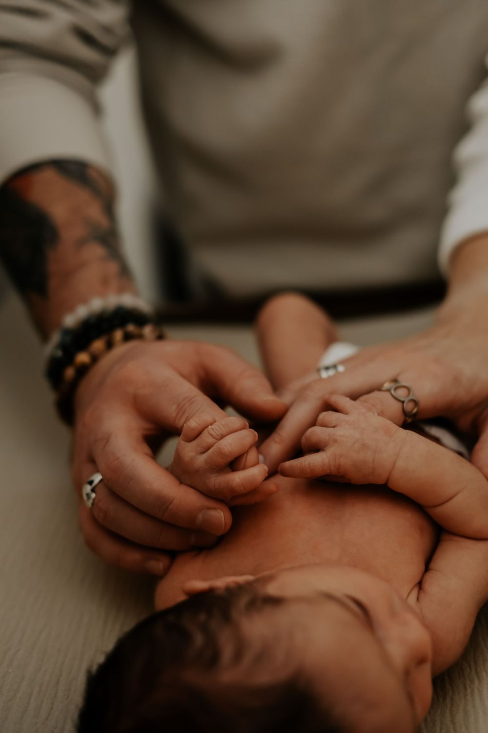 Close up of hands holding newborn baby with bracelet and rings visible.