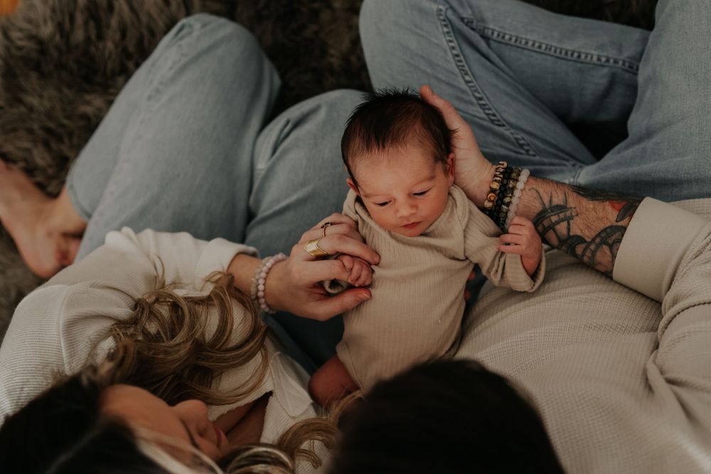 Family cuddles with newborn baby on couch during intimate lifestyle photography session.