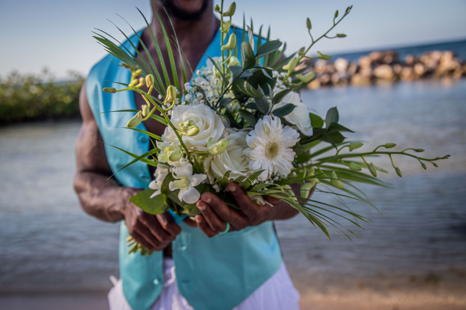 White and green wedding bouquet held against turquoise beachwear.