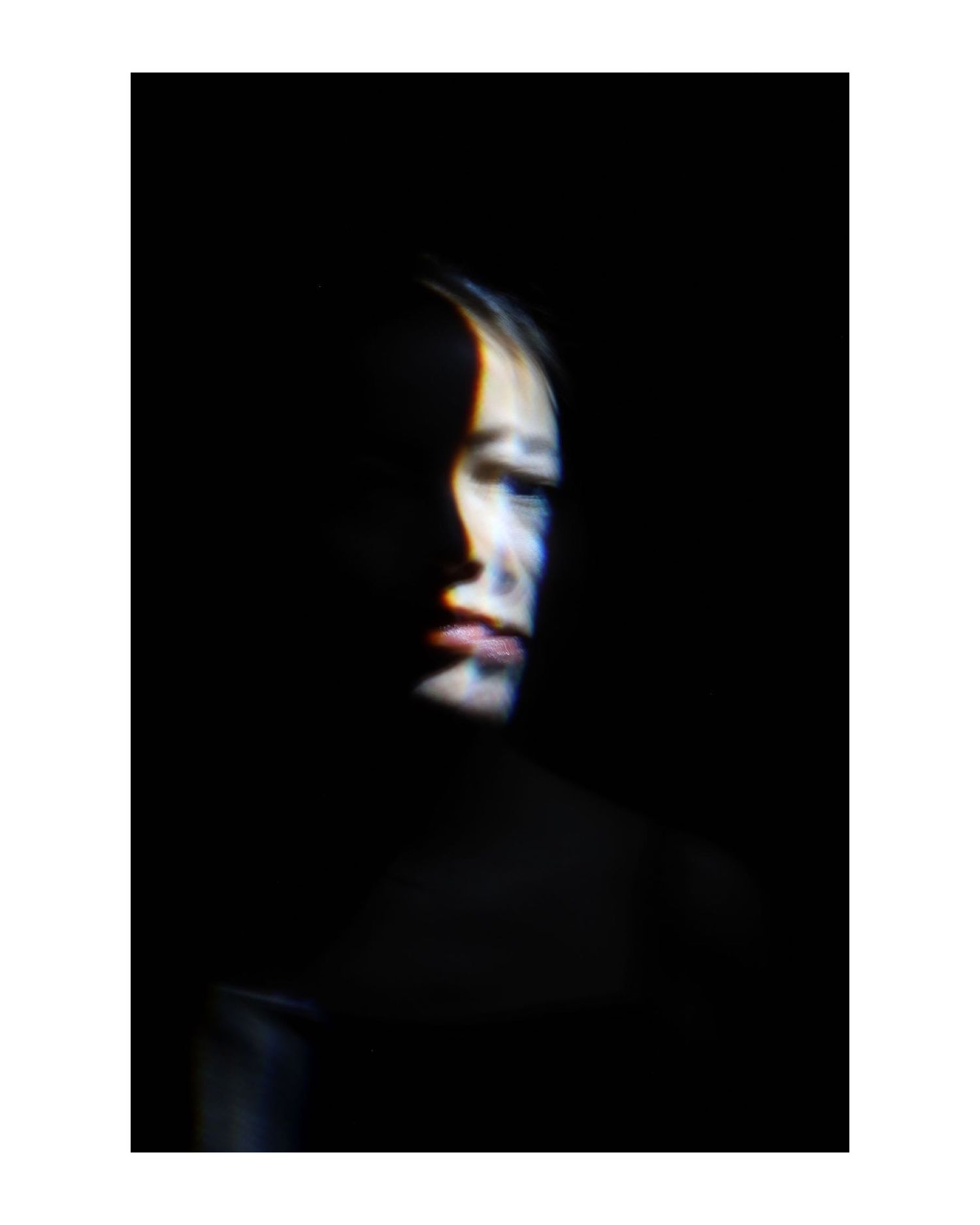 Dramatic portrait with half-lit face against black background.