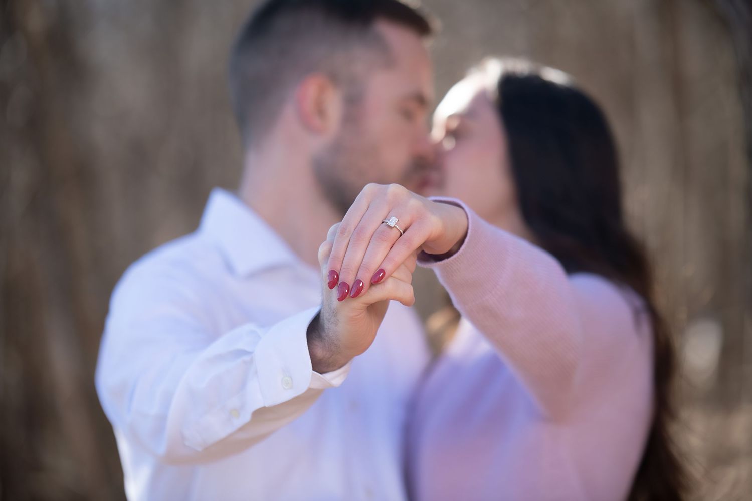 Close-up engagement ring display with couple sharing intimate moment in background.
