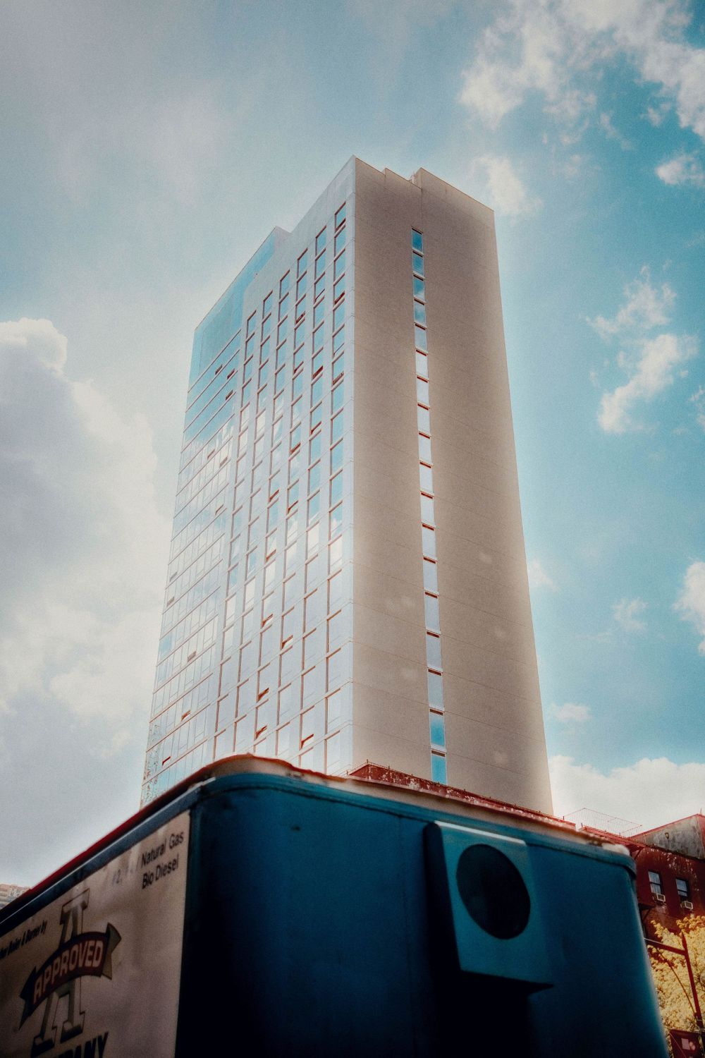 Modern high-rise building photographed from below against blue sky with clouds.