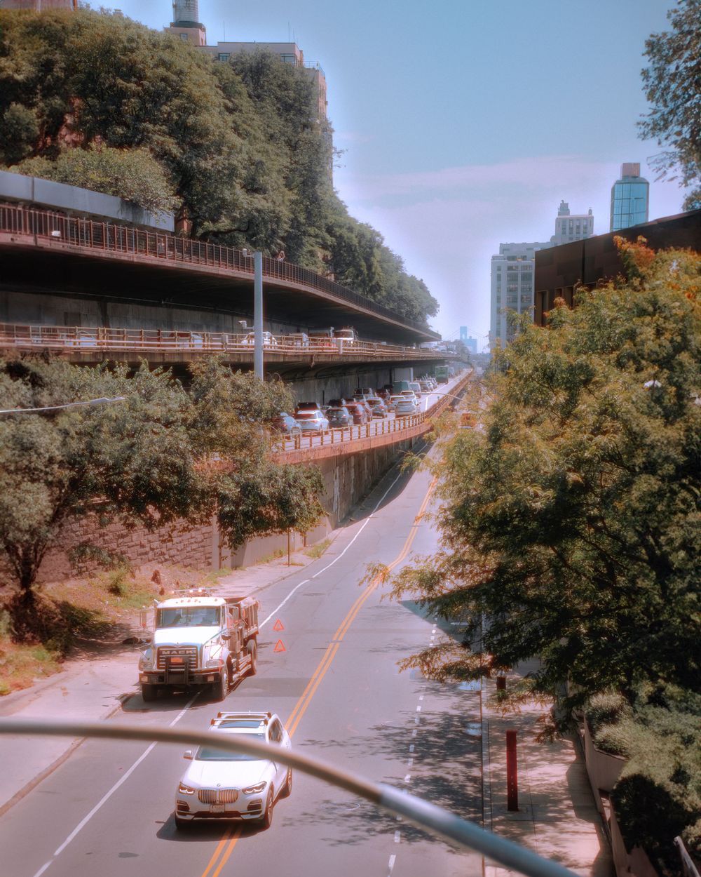 Curved elevated roadway through city trees with vehicles below.