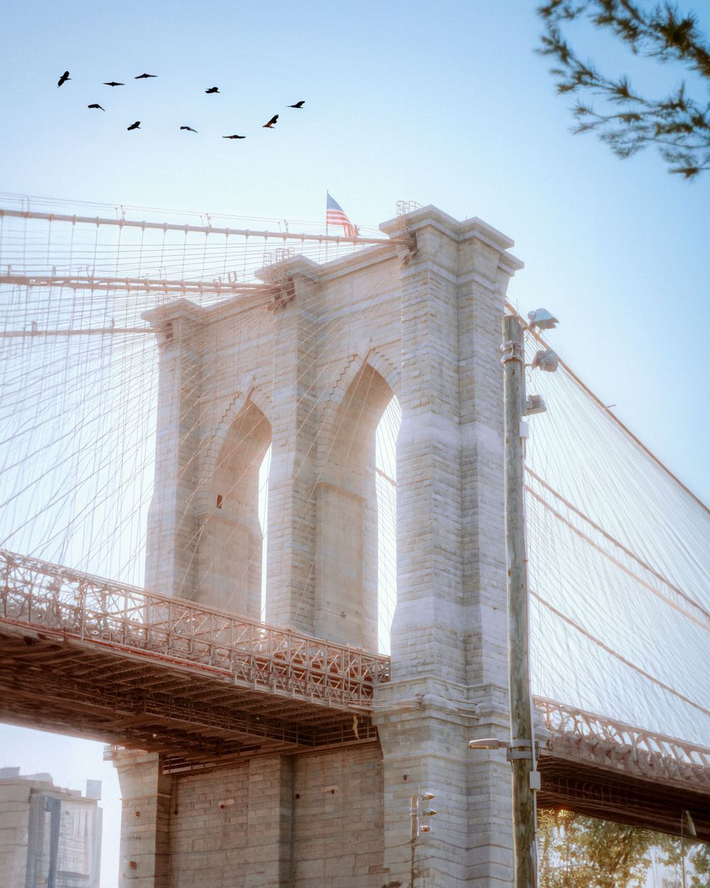 Birds fly over the Brooklyn Bridge tower with an American flag waving in the misty sky.