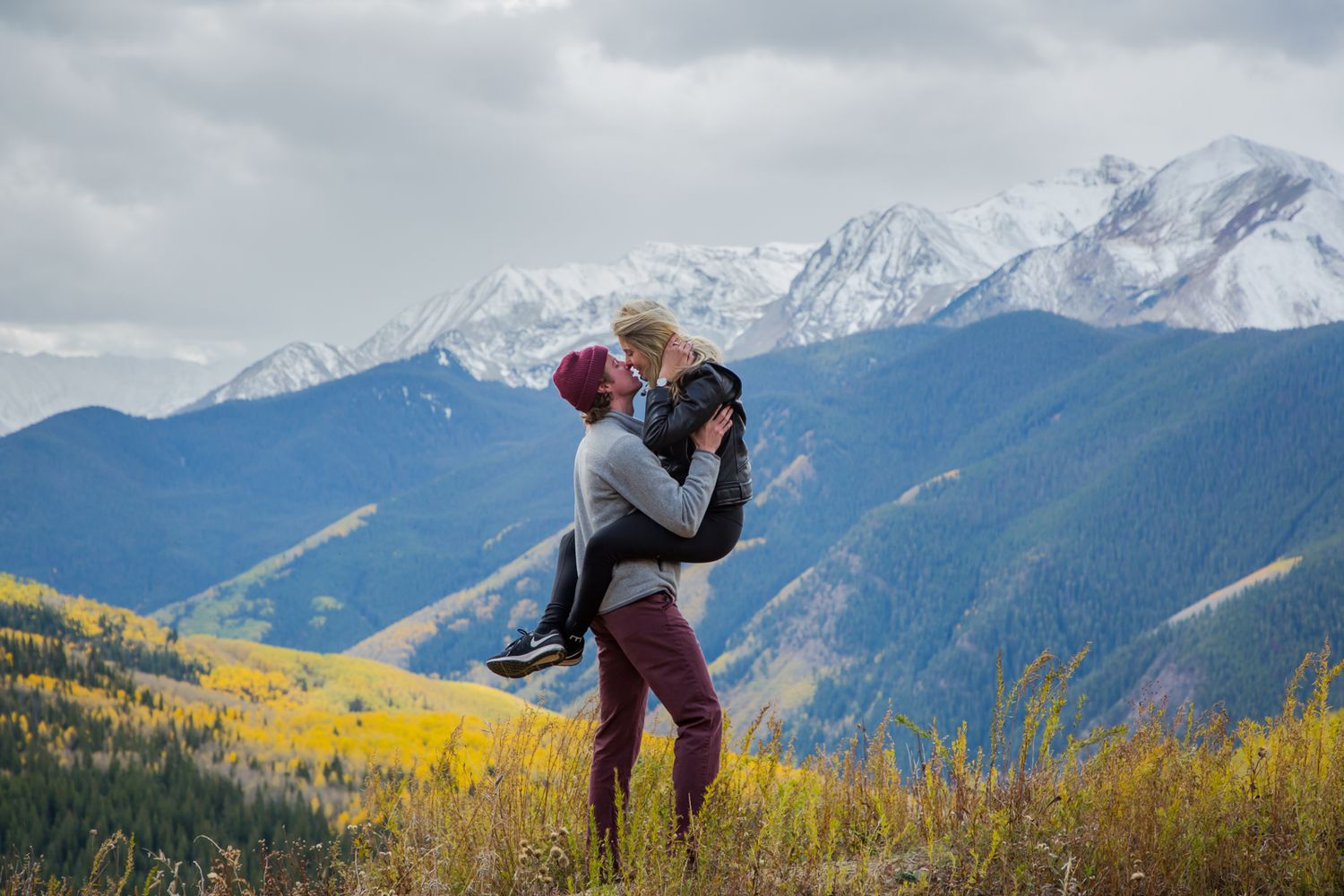 A couple sharing a romantic moment against a backdrop of majestic mountain peaks and autumn colors.