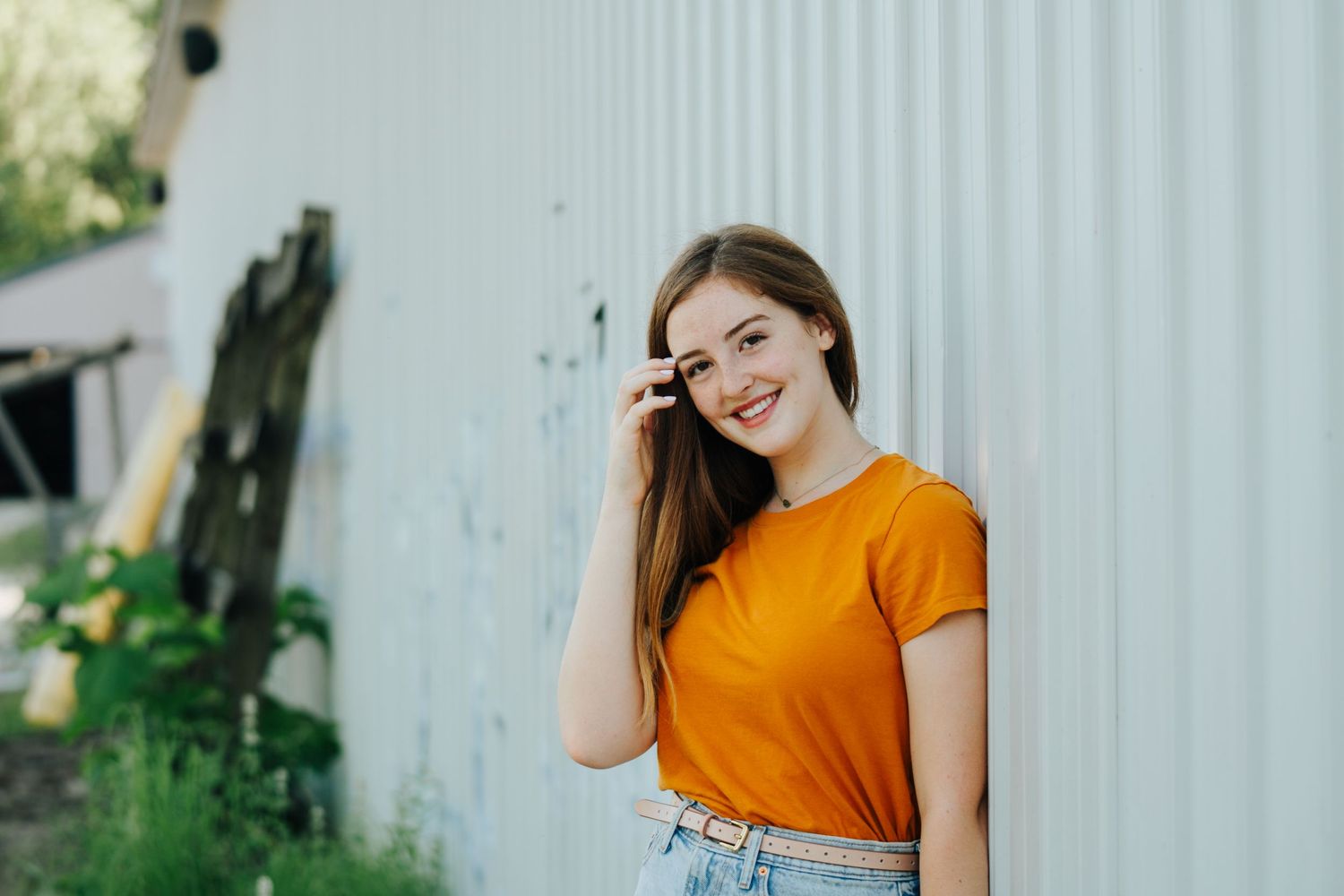 Person in orange shirt posing against white corrugated wall outdoors.