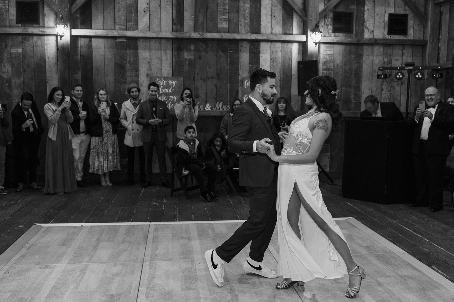 A black and white photo captures a romantic dance moment in a rustic barn setting.