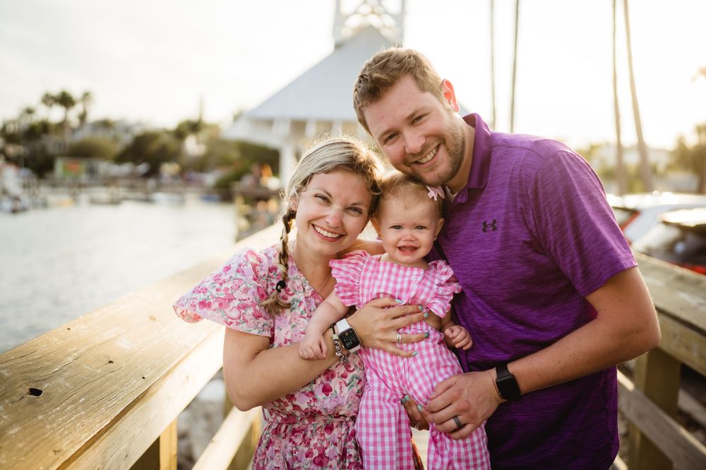 A family of three poses together on a wooden dock at sunset near a marina.