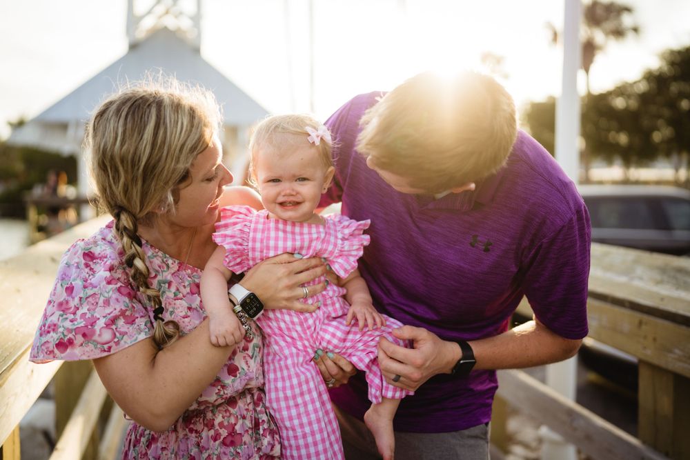 A tender family moment shared on a sunny pier with a white tower in the background.