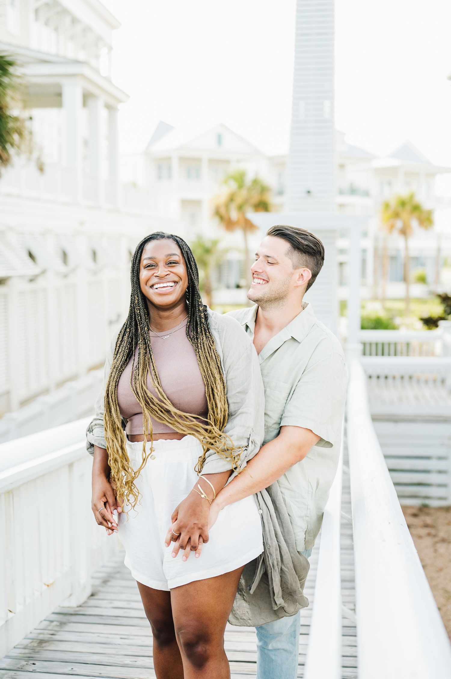 Happy couple sharing intimate moment on coastal boardwalk during sunny day.