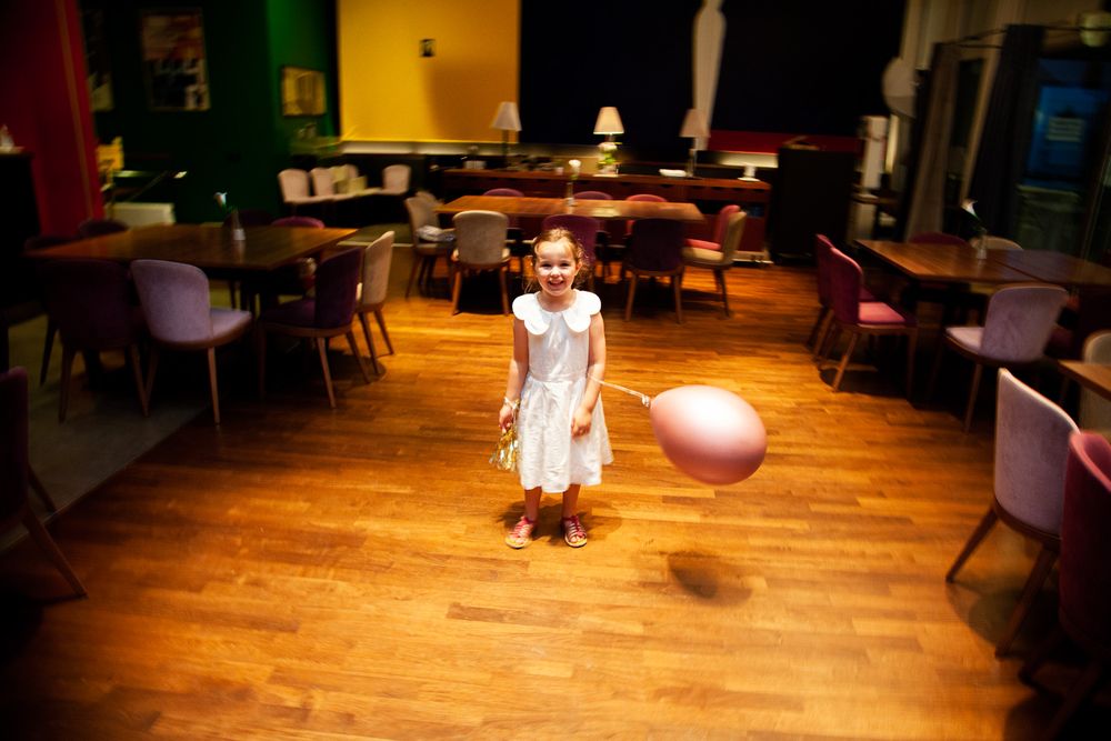 A child playing with a balloon in an empty dining room with wooden floors and chairs.
