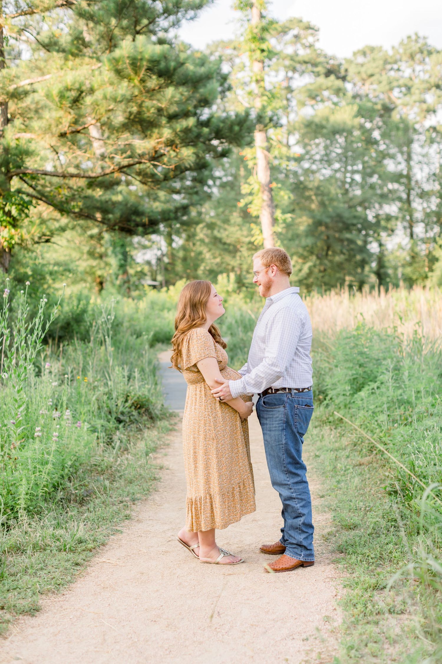 Couple shares a tender moment on a dirt path surrounded by pine trees.