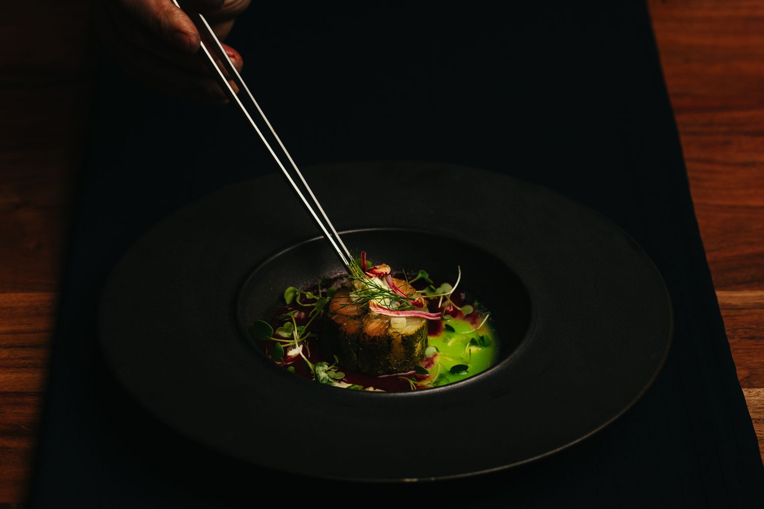 Fine dining dish presentation on black plate with precise garnishing.
