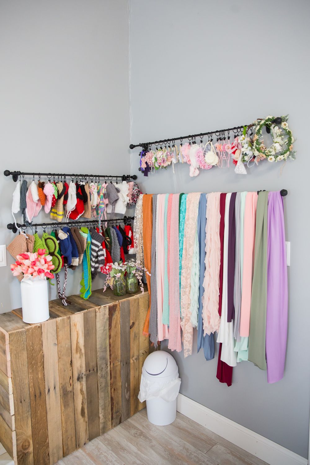 Photography studio corner with clothing rack, floral decorations, and fabric backdrops in pastel colors.
